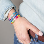 Stack of colorful resin tile bracelets on a wrist with gold accents.