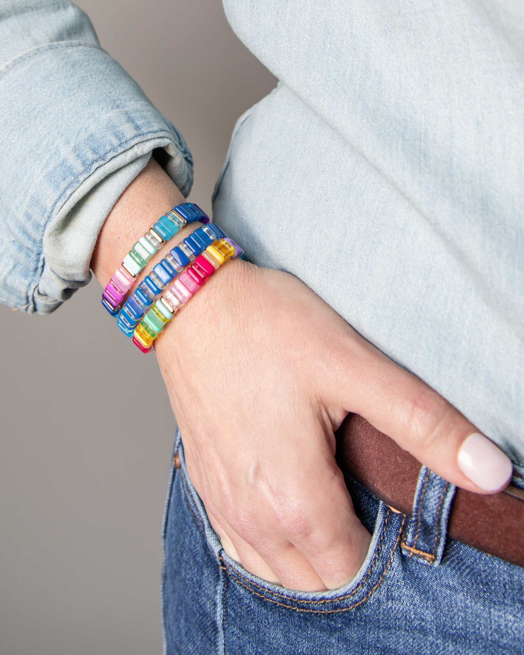 Stack of colorful resin tile bracelets on a wrist with gold accents.