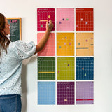 Woman writing on a monthly wall calendar in rainbow colors hanging on a white wall.