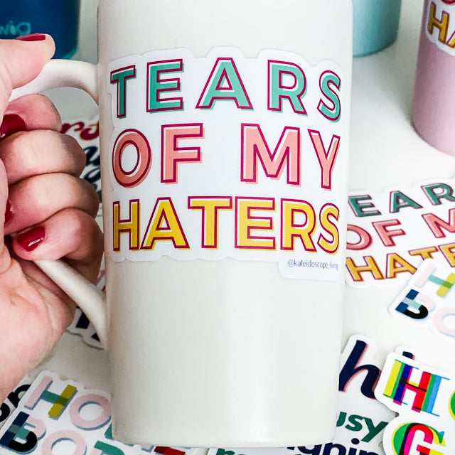Close up picture of a sticker reading "TEARS OF MY HATERS" on a white mug.