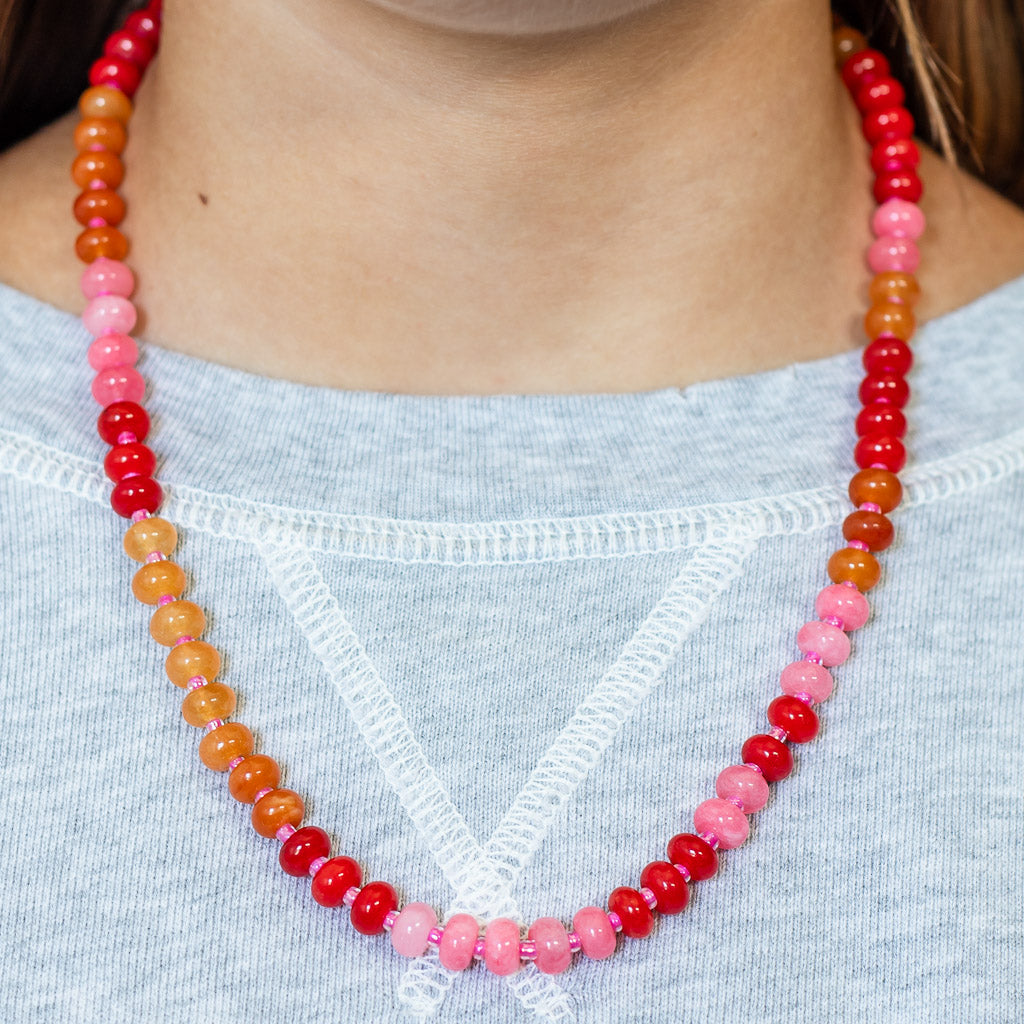 Close up of a natural stone beaded necklace in shades of red, pink and orange from Kaleidoscope Living.