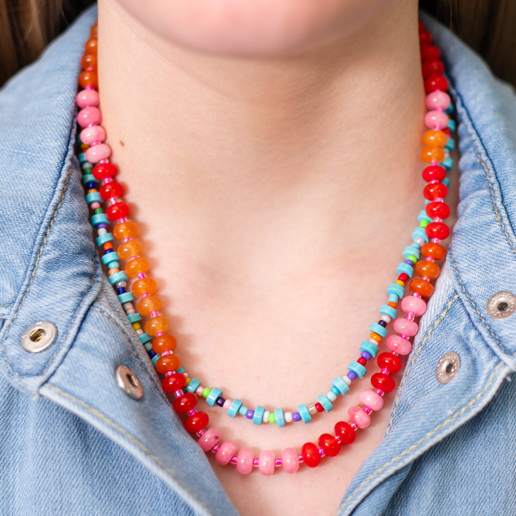 Girl wearing two natural stone beaded necklaces in vibrant colors of red, pink, orange and blues.