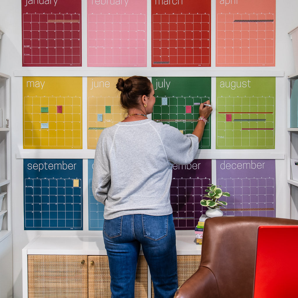 woman writing on large, undated reusable wall calendar in colorful rainbow hues from Kaleidoscope Living