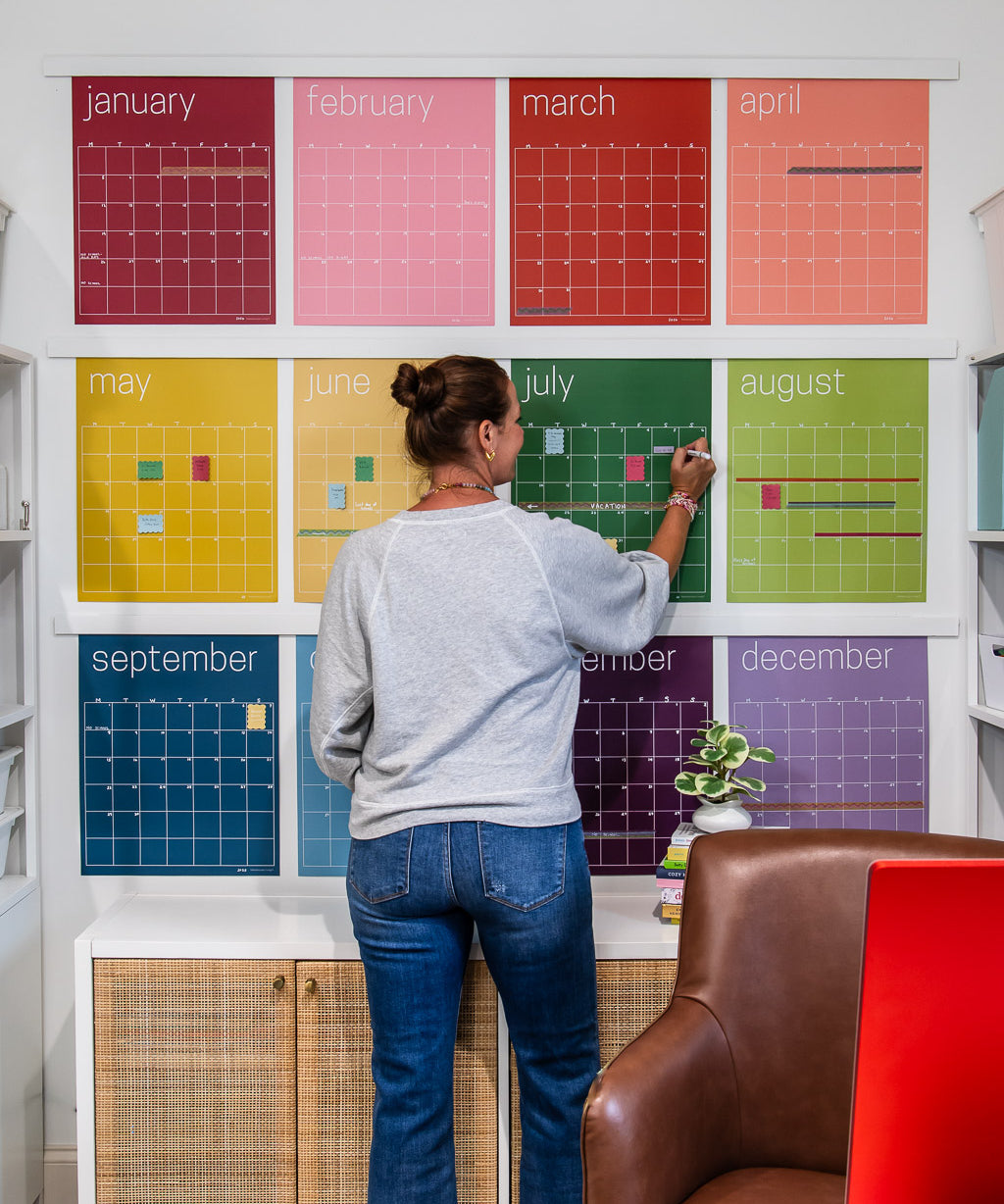 woman writing on large reusable wall calendar in colorful rainbow hues from Kaleidoscope Living