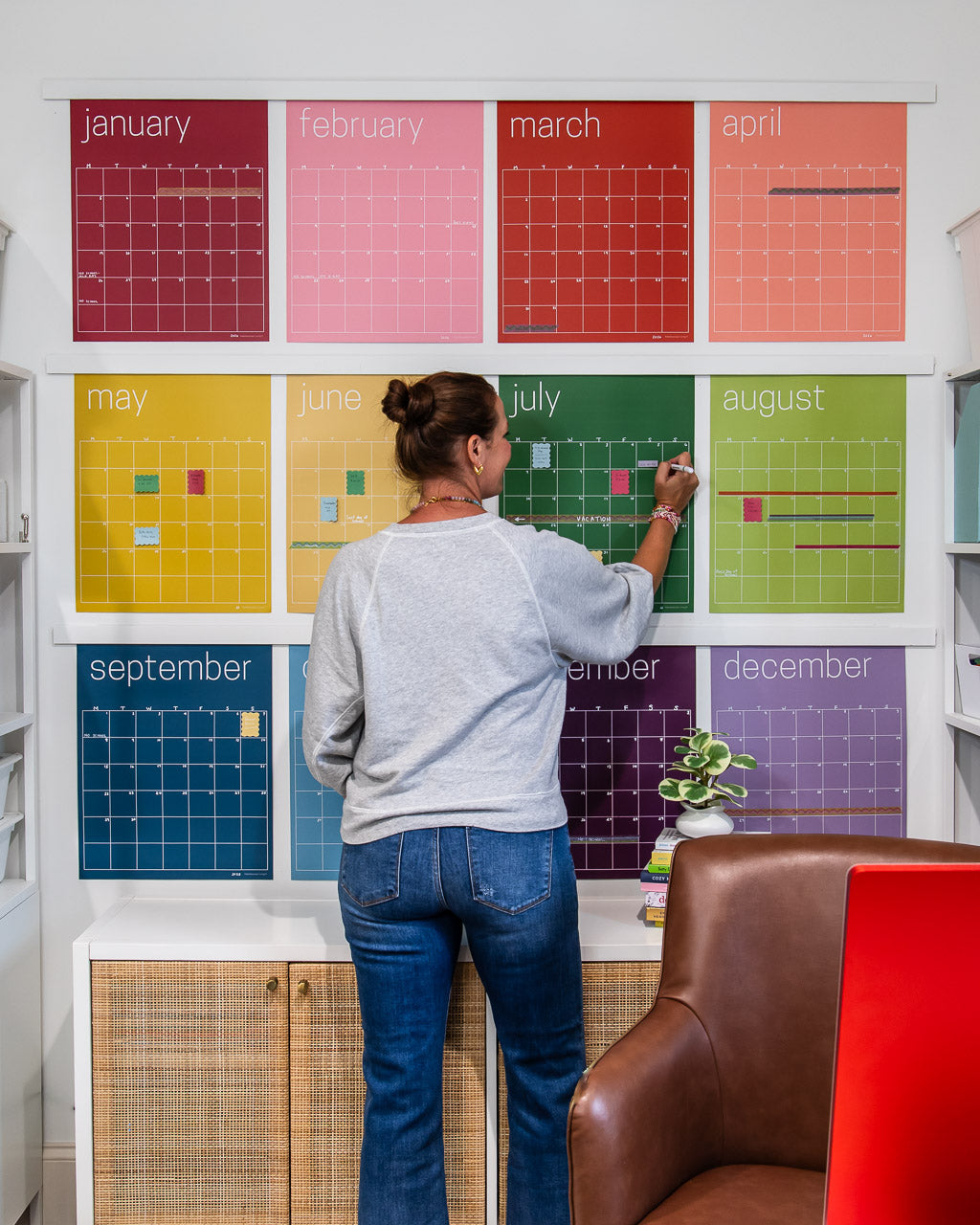 woman writing on large reusable wall calendar in colorful rainbow hues from Kaleidoscope Living