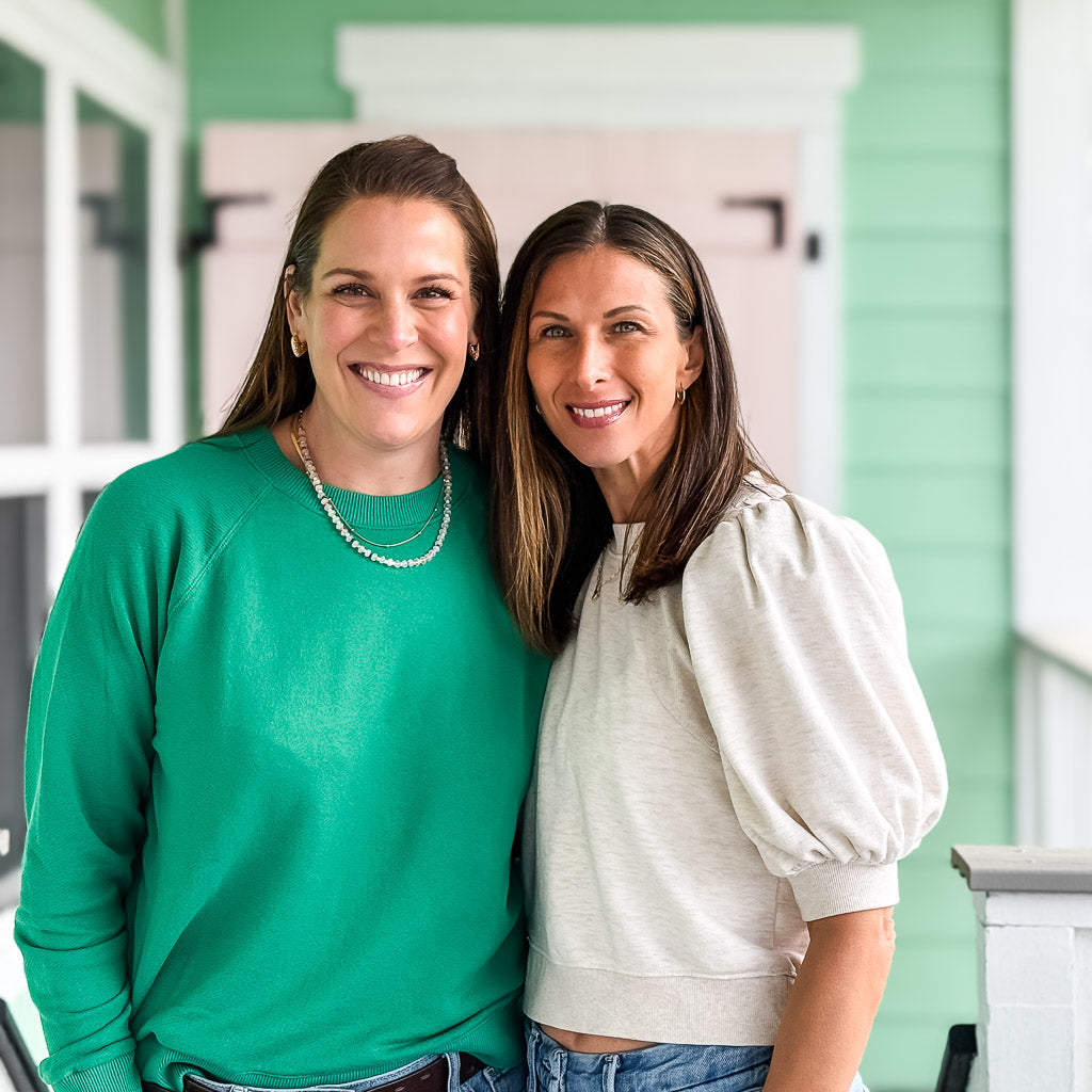 Two women, from Kaleidoscope Living, standing side by side on a porch with a green wall in the background.