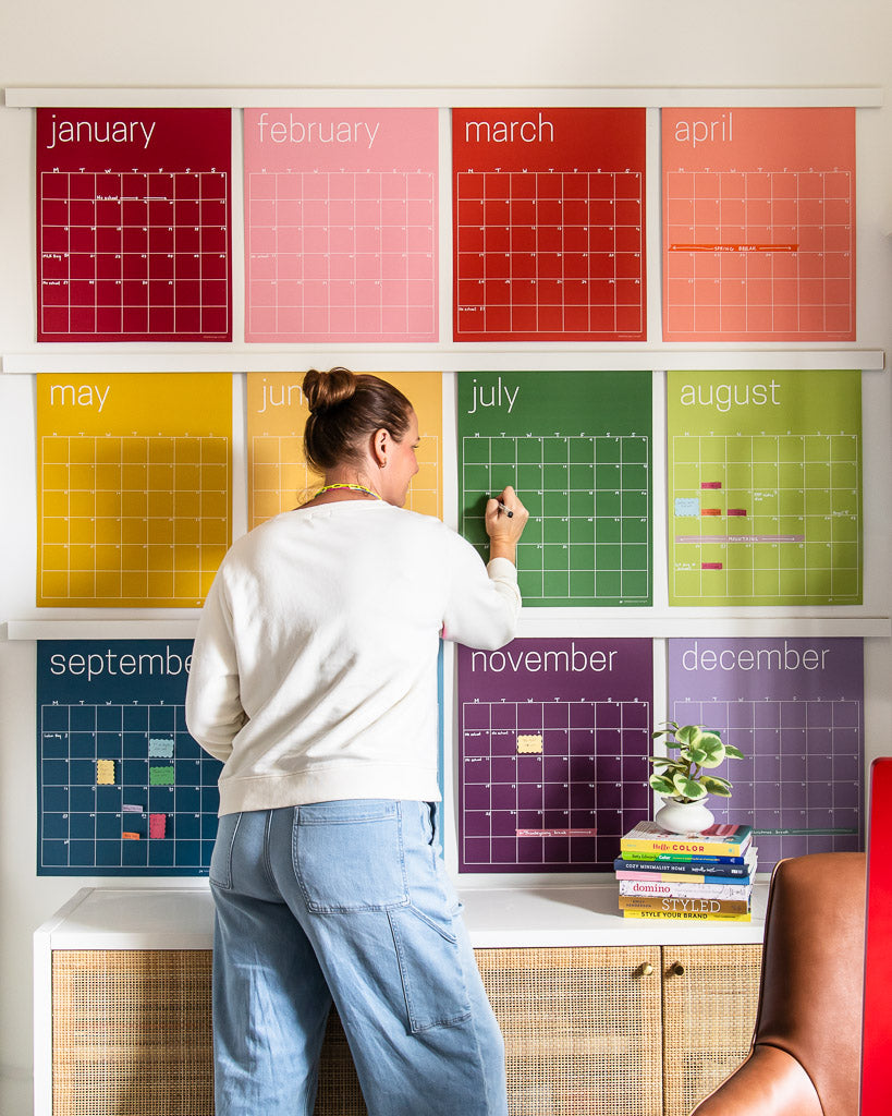 woman writing on large wall calendar in colorful rainbow hues from Kaleidoscope Living