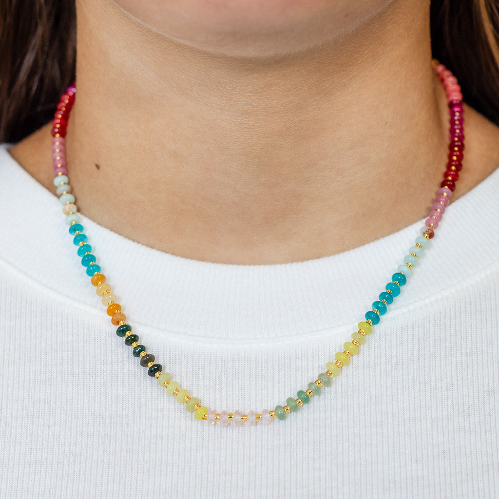 Close up of a colorful necklace with petite natural stone beads in vibrant sunset hues and gold accents.