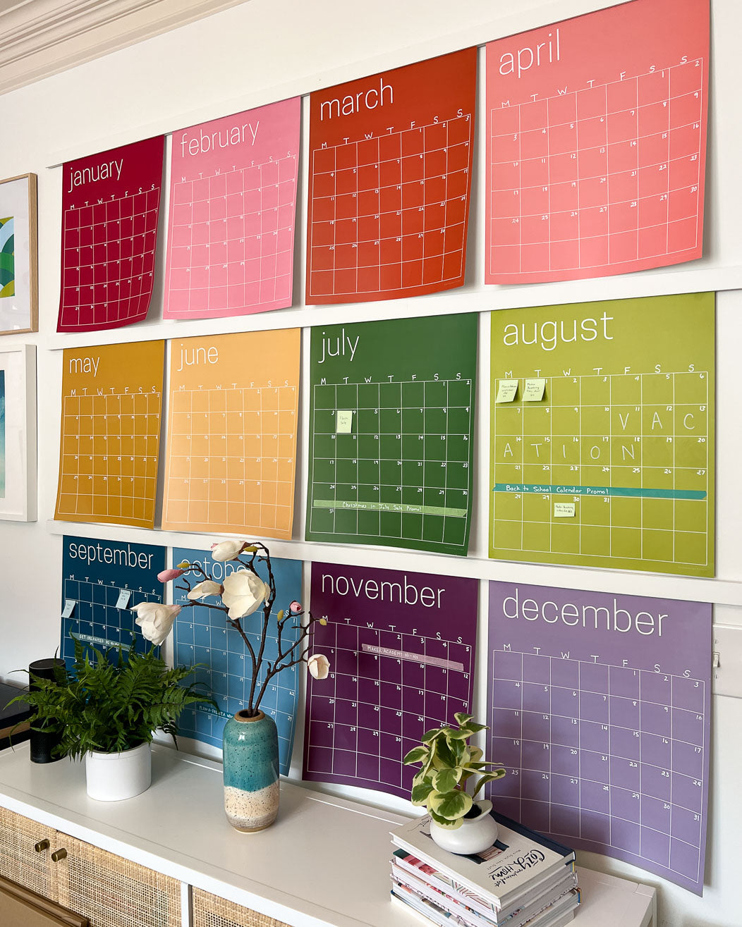 Rainbow erasable monthly wall calendar with twelve large monthly pages hanging on white wall above console table