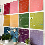 Rainbow erasable monthly wall calendar with twelve large monthly pages hanging on white wall above console table
